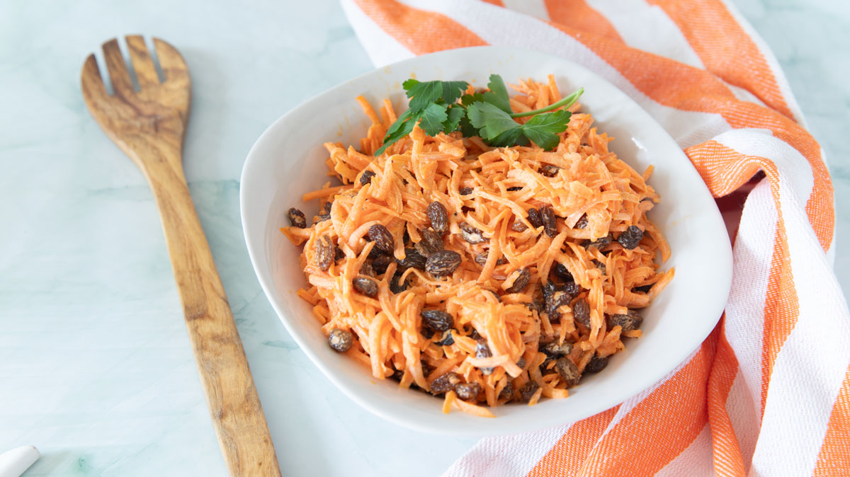 Carrot salad in a white serving bowl with a serving spoon.