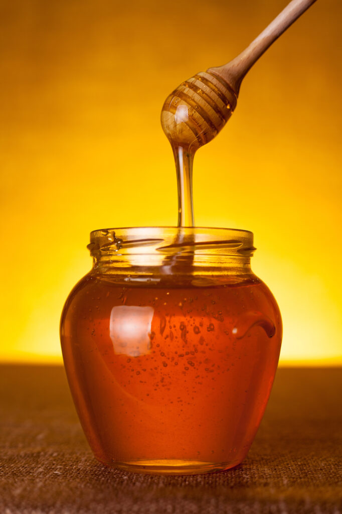 Honey dipper dripping honey into a jar.