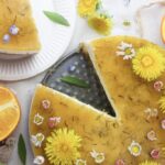 An overhead of a Orange Dandelion Cake with a slice on the side and oranges around.