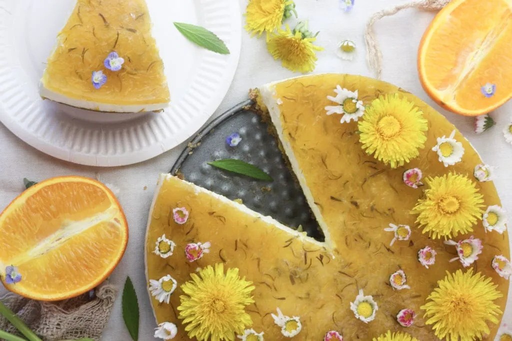 An overhead of a Orange Dandelion Cake with a slice on the side and oranges around.