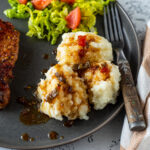 Pork chop with candied jalapeños on a gray plate with potates and salad..