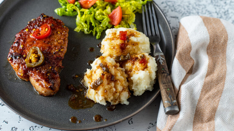 Pork chop with candied jalapeños on a gray plate with potates and salad..
